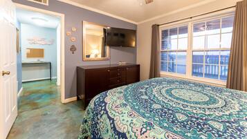 Une chambre avec un grand lit, une commode, un téléviseur et une fenêtre avec des rideaux.