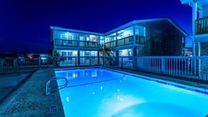 A multi-story hotel with a swimming pool, outdoor lighting, and a fenced deck area. - Waterfront Condo: Stunning Sunsets, Fishing, Pool, Private Patio, Near Beach  (Corpus Christi)