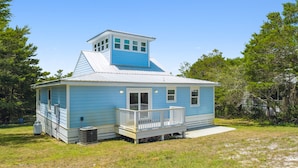 A small, single-story house with a blue exterior and white trim, featuring a front porch and a small tower-like structure on the roof. - 30A Beach House - Vitamin Sea by PHG (Santa Rosa Beach)