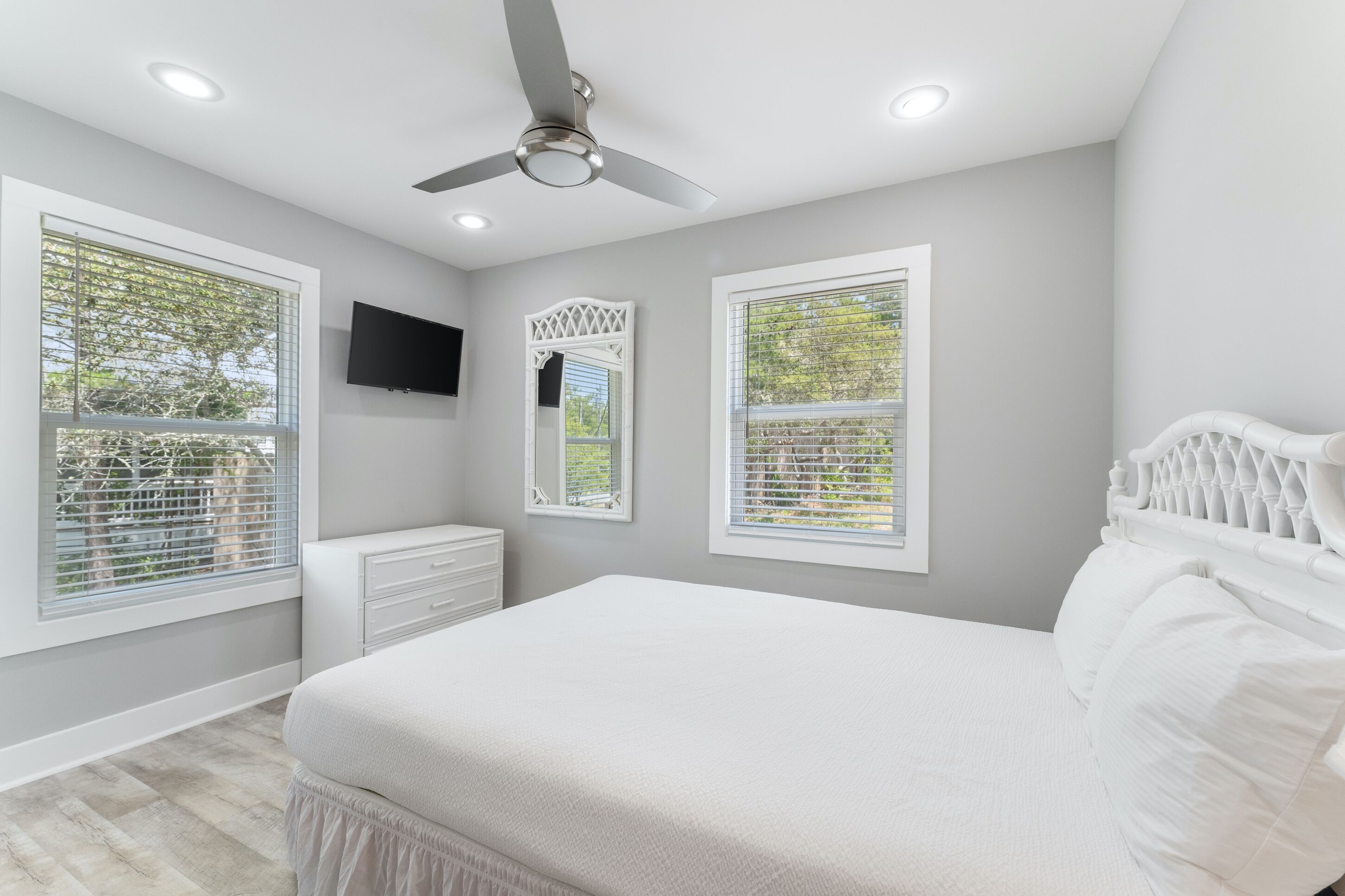 A bedroom with a bed, a ceiling fan, a TV, and windows with blinds.