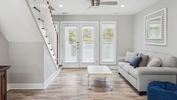 A modern living room with a staircase, white walls, a ceiling fan, and a light-colored sofa. - 30A Beach House - Vitamin Sea by PHG (Santa Rosa Beach)