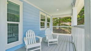 A covered porch with two white Adirondack chairs, a railing, and a view of greenery. - 30A Beach House - Vitamin Sea by PHG (Santa Rosa Beach)