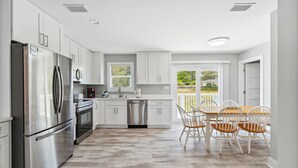 A modern kitchen with white cabinets, stainless steel appliances, and a dining area with a wooden table and chairs. - 30A Beach House - Vitamin Sea by PHG (Santa Rosa Beach)
