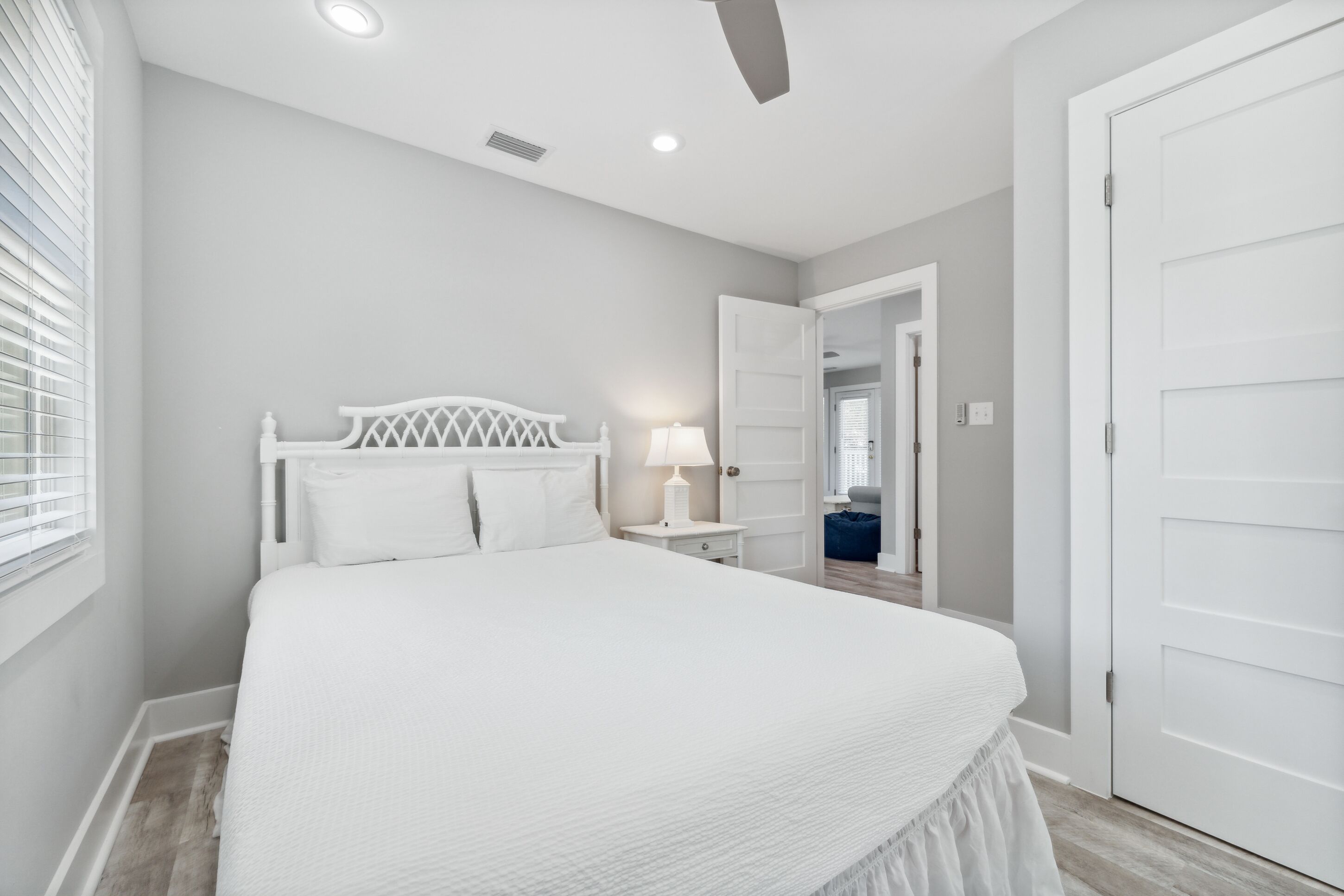 A bedroom with a large bed, white headboard, bedside table with a lamp, and a door leading to another room.