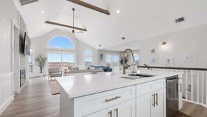 A spacious kitchen with white cabinetry, a large island, and a view to the outdoors. - Relaxing Oceanfront Retreat | Pool, Hot Tub & Beach - Sleeps up to 14! (Rodanthe)