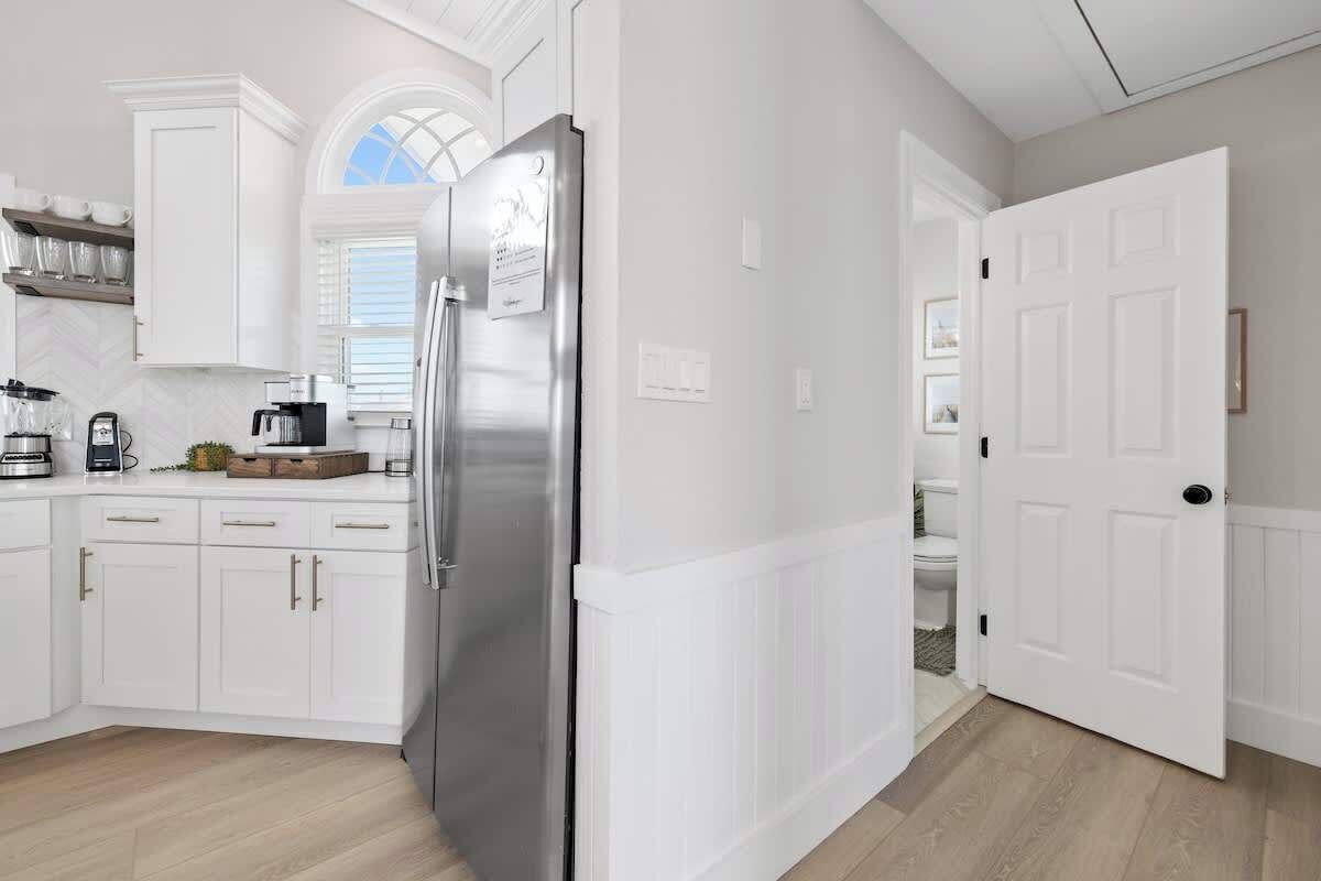 A modern kitchen with white cabinetry, a stainless steel refrigerator, and a window with a view.