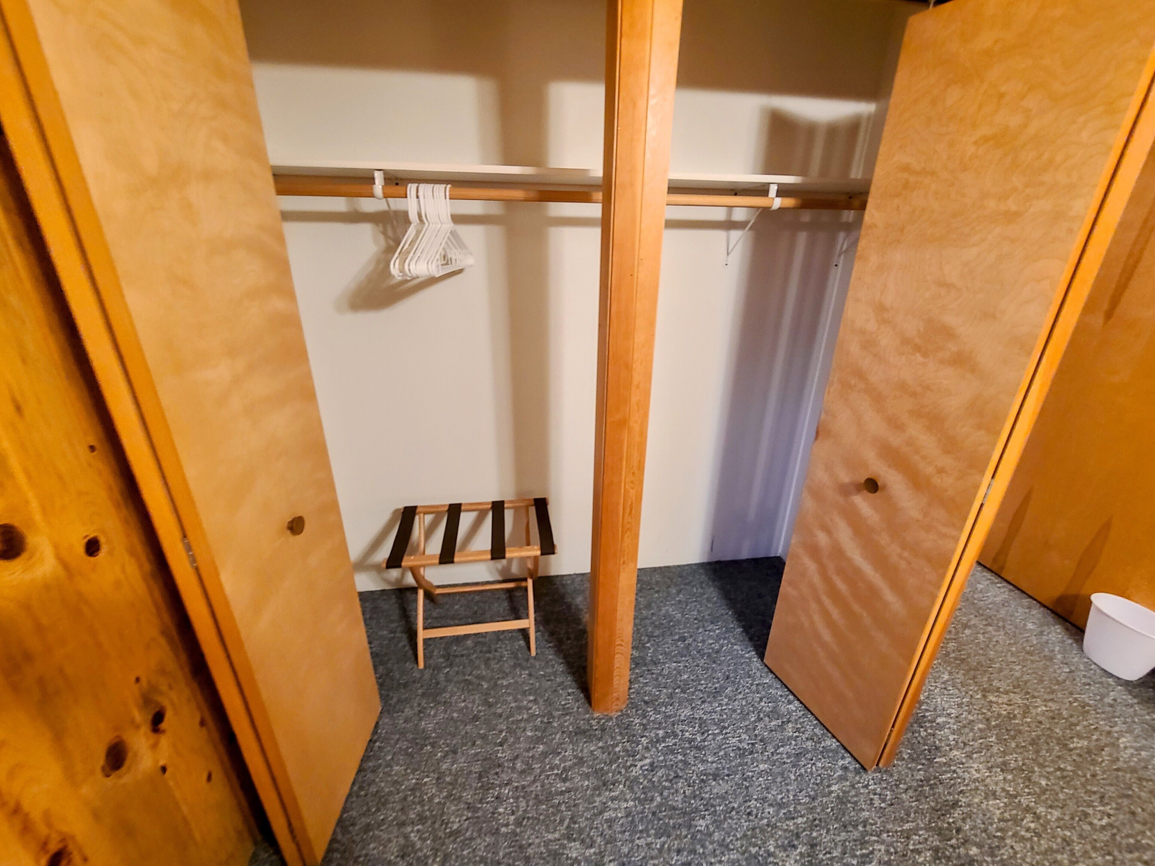 A small, compact room with a wooden wardrobe, a small stool, and a hanging rack.