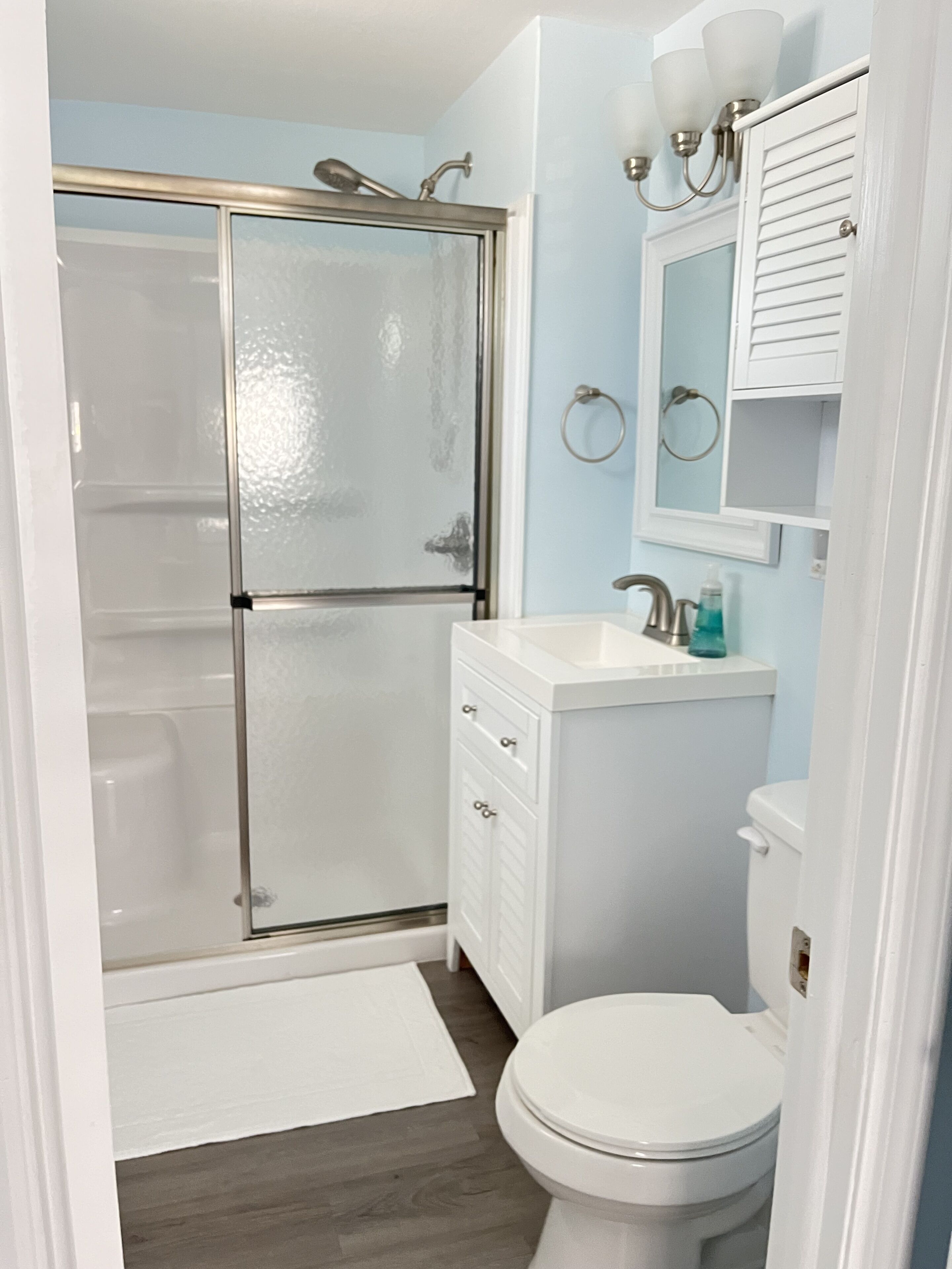 Ein Badezimmer mit Duschkabine aus Glas, einem weißen Waschbecken, einer Toilette und einem Spiegel über dem Waschbecken.