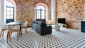 A modern living room with a stone wall, a black sofa, a dining table with chairs, and a TV. - Lefevre 1C (Panama City)