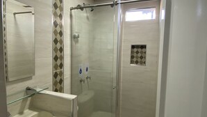 Une salle de bain moderne avec une douche à parois de verre, des toilettes blanches et une étagère en verre.