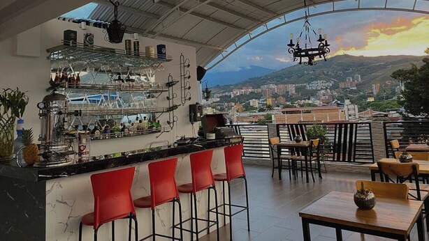 Un espace bar avec vue sur la ville, des tabourets de bar rouges et une table avec des chaises.
