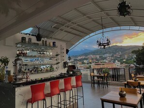 Eine Bar mit Blick auf die Stadt, rote Barhocker und ein Tisch mit Stühlen.