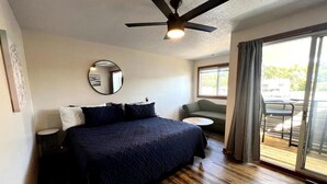 Een slaapkamer met een bed, een ronde spiegel, een plafondventilator, een klein rond tafeltje en uitzicht op de buitenlucht via een schuifdeur van glas.