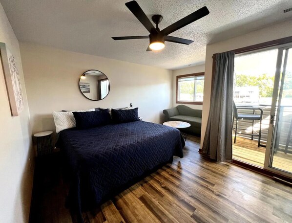 Une chambre avec un lit, un miroir rond, un ventilateur de plafond, une petite table ronde et une vue sur l’extérieur grâce à une porte-fenêtre coulissante.
