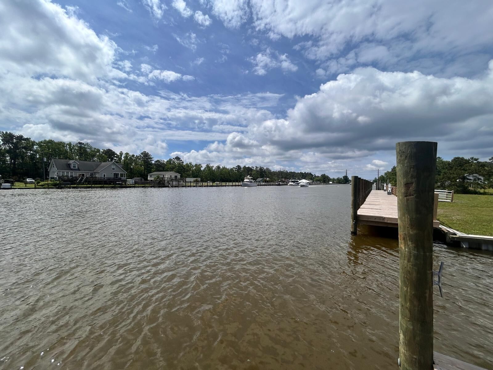 Een rustige rivier met een houten steiger die in het water reikt, omringd door een woongebied met huizen en bomen.