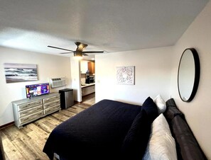 Une chambre à coucher comprenant un lit, un ventilateur de plafond, une télévision, une commode et des œuvres d’art accrochées aux murs.