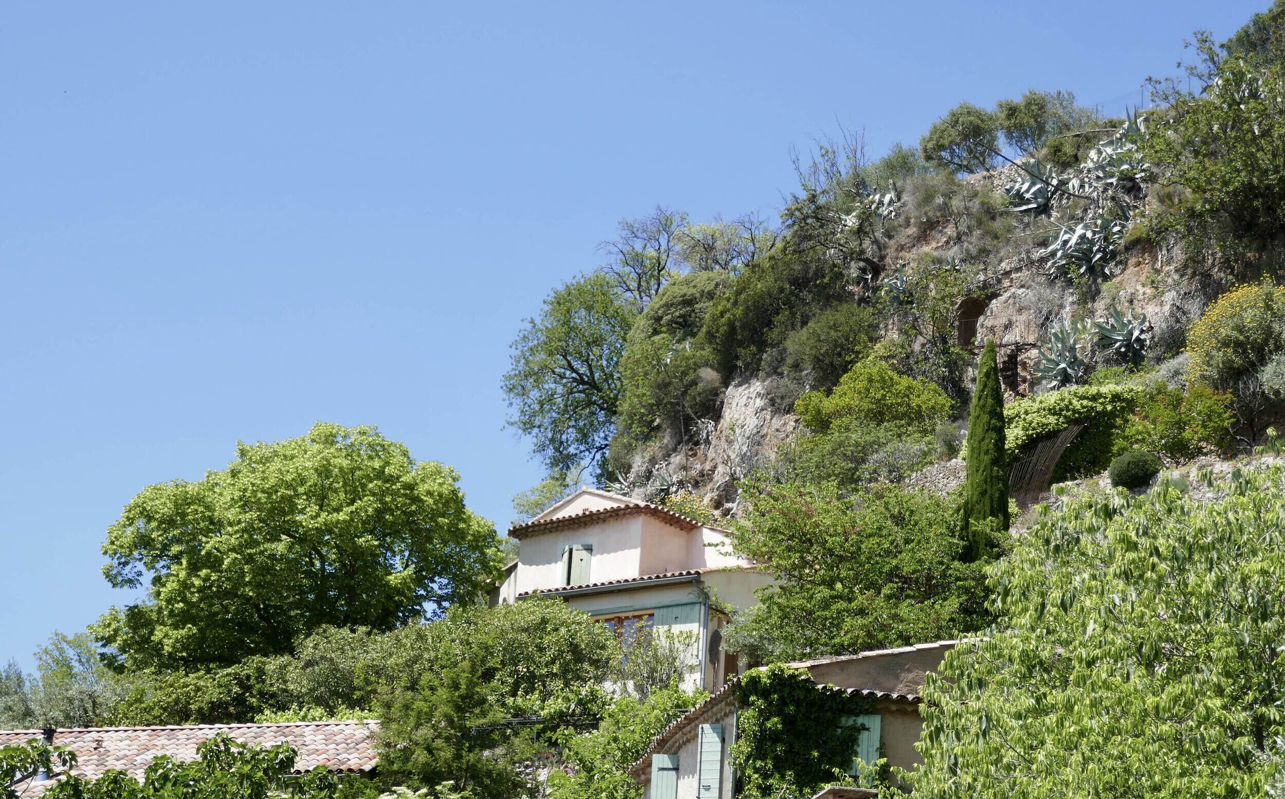 Un edificio con tetto in tegole, circondato da vegetazione rigogliosa e un pendio roccioso.