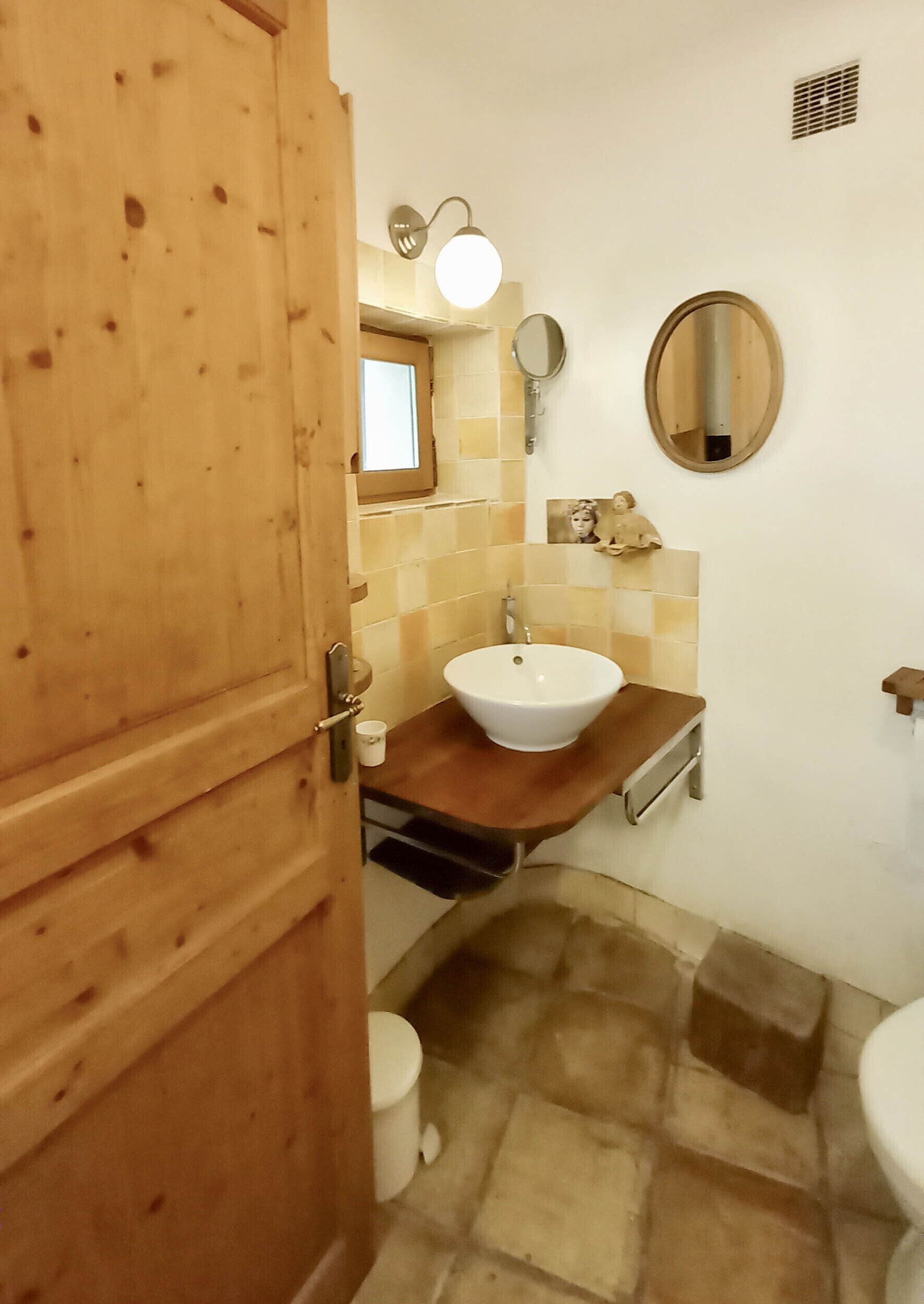 Une salle de bain avec une porte en bois, un lavabo blanc, un miroir et des toilettes.