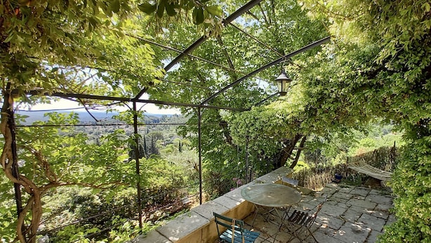 Une terrasse couverte, dotée d’une table et de chaises, entourée d’une végétation luxuriante et offrant une vue sur le paysage.