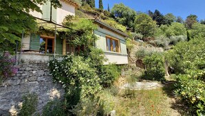 Une maison de campagne en pierre, avec un jardin, un mur de pierre et un ciel d’un bleu éclatant.