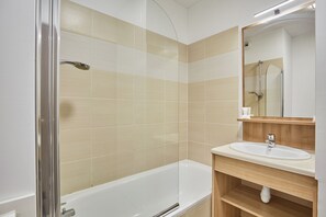 Un baño moderno con ducha envuelta en vidrio, una bañera blanca y un mueble de tocador de madera con lavamanos.