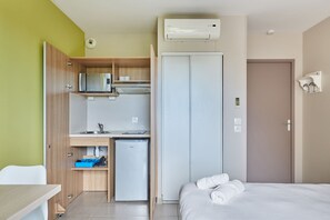 Una habitación de hotel compacta con kitchenette, una cama y un armario.