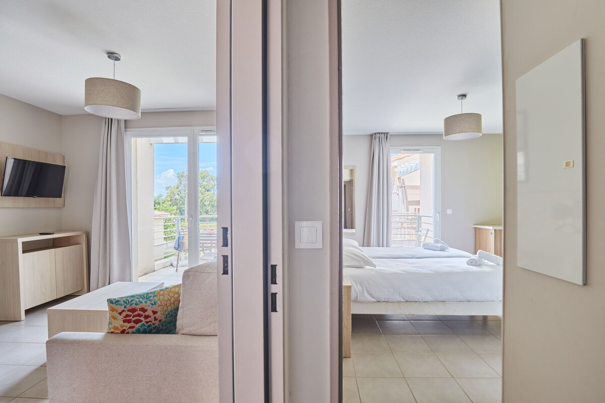 Una habitación de hotel moderna con sofá, cama, televisión y balcón con cortinas.