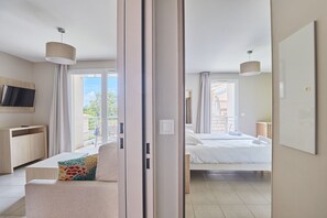 Una habitación de hotel moderna con sofá, cama, televisión y balcón con cortinas.