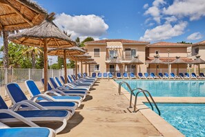 Zona junto a la piscina con sillas de descanso y sombrillas, una piscina y un edificio con tejado de baldosas.