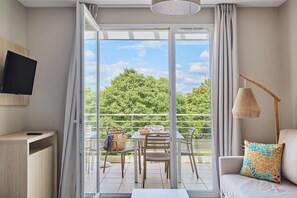 Habitación moderna con puerta de vidrio corredera que da a un espacio exterior. Hay un sofá con un cojín colorido, una mesa con sillas y un televisor montado en la pared.
