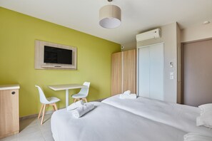 Una habitación de hotel con cama, escritorio, dos sillas, televisor y armario.