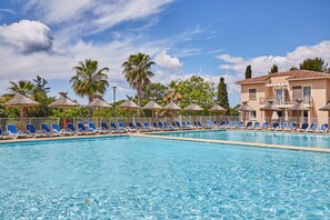 Una piscina con sillas de descanso y palmeras al fondo.