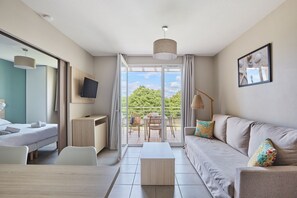 Habitación de hotel moderna con cama, escritorio, sofá y balcón con mesa y sillas.