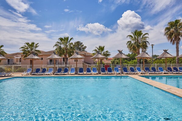 A swimming pool with blue water, surrounded by lounge chairs and palm trees.