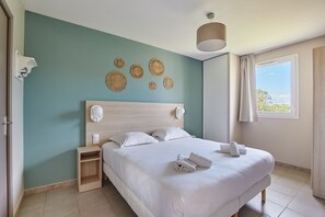 Un dormitorio ordenado con una cama grande, una mesita de noche y una lámpara fijada a la pared.