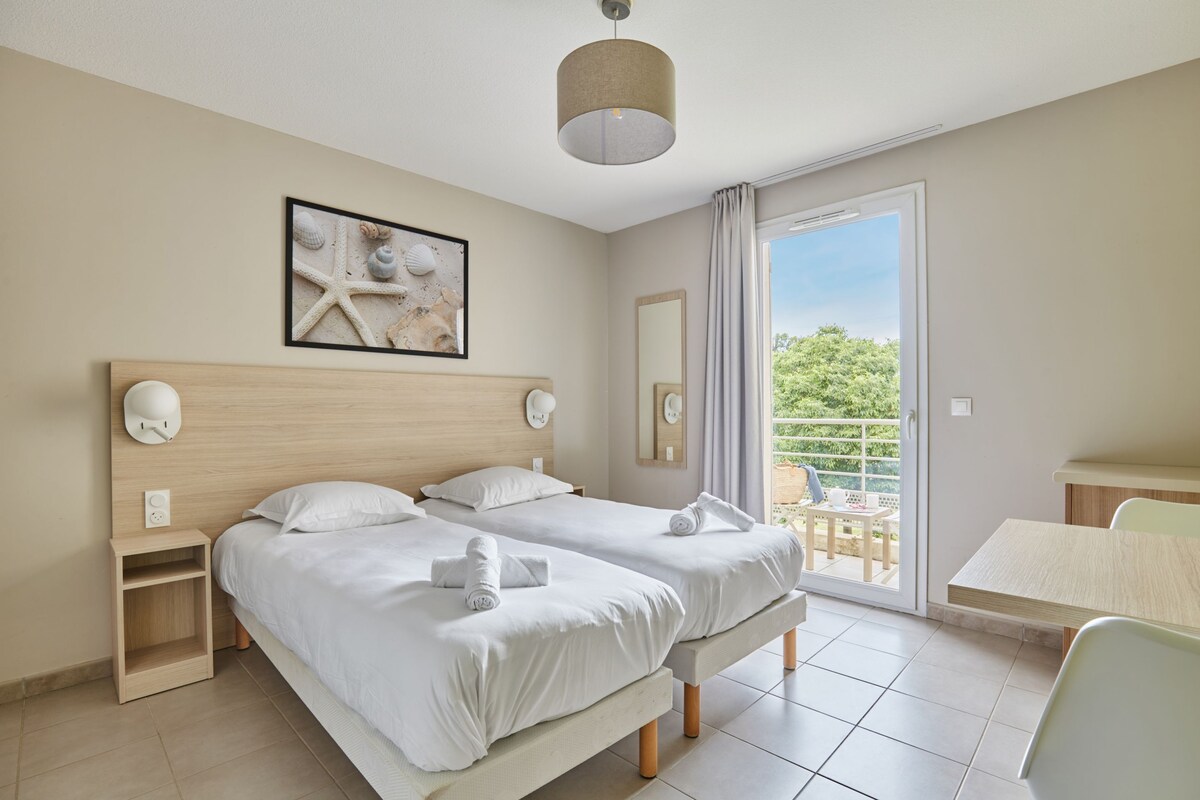 Habitación de hotel con dos camas, un balcón, una mesa y una silla.