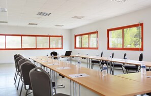 Ein Konferenzraum mit langen Tischen, Stühlen und großen Fenstern mit Jalousien.