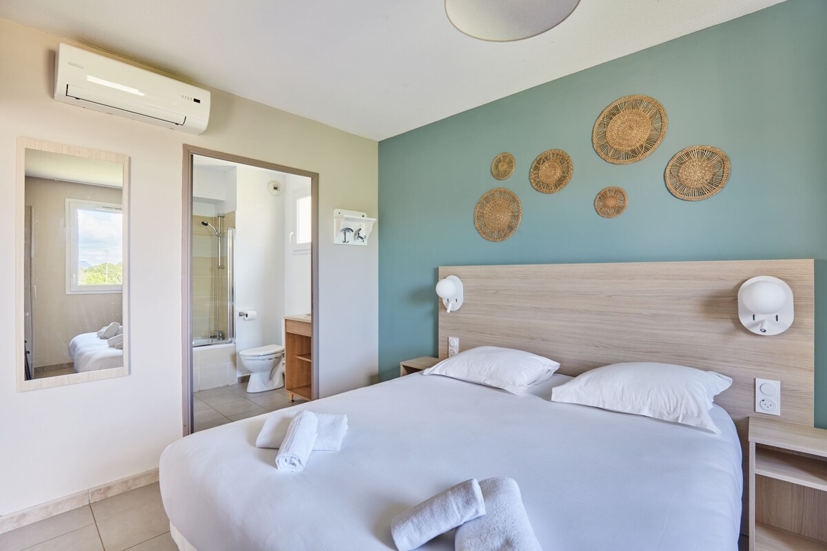 Una habitación de hotel con una cama grande, un baño con ducha y un espejo.