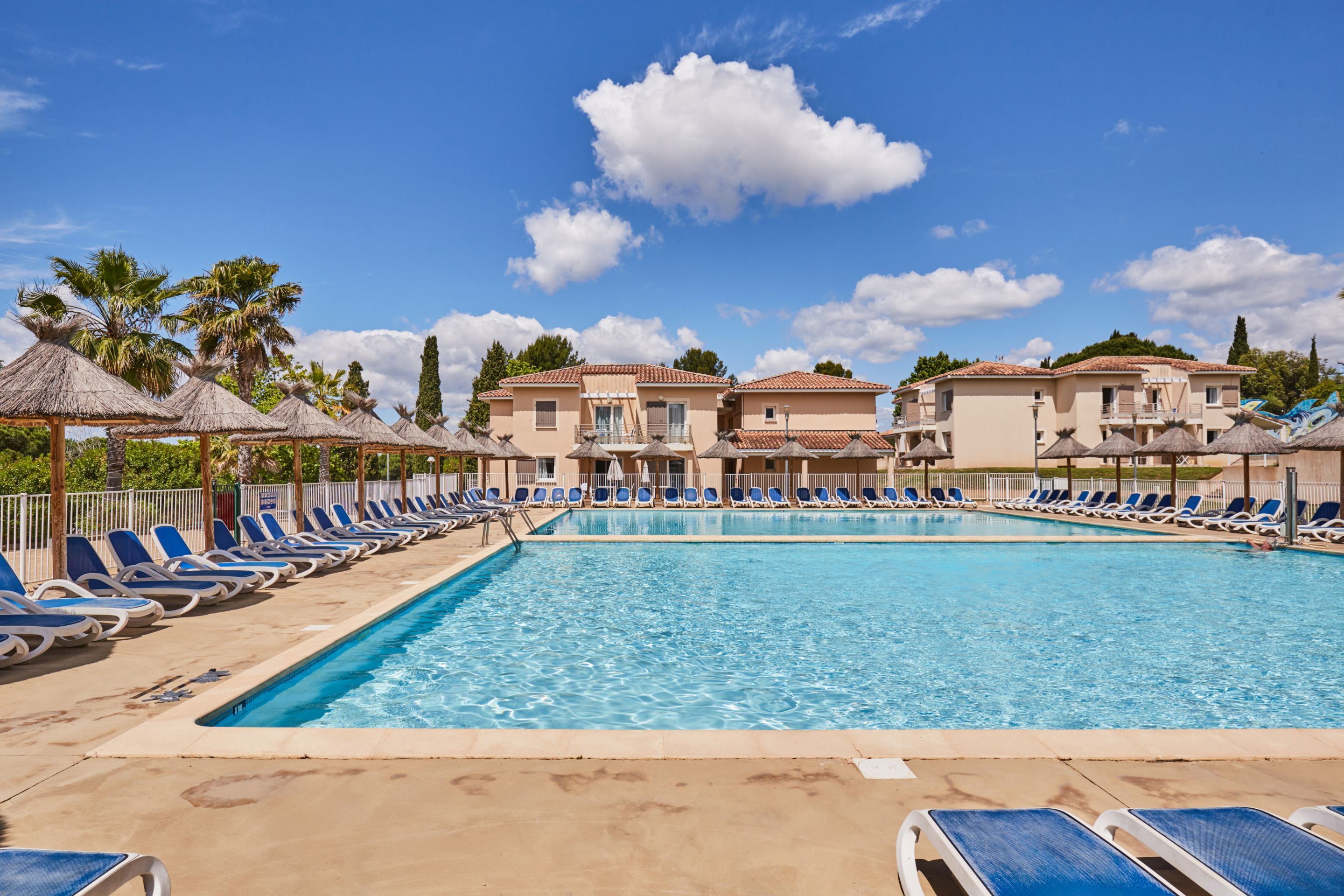 A swimming pool with lounge chairs and umbrellas, surrounded by buildings with balconies.