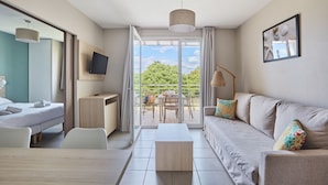 A modern hotel room with a bed, a desk, a sofa, and a balcony with a table and chairs. - Residence Odalys Les Oceanides (La Londe-les-Maures)