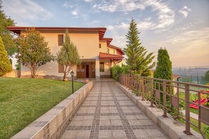 A two-story house with a tiled pathway leading to the entrance, surrounded by greenery and a view of the landscape. - Park hotel Arbanasi (Veliko Tarnovo)
