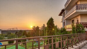 A residential building with a balcony, a fenced garden with a trampoline, and a sunset in the background. - Park hotel Arbanasi (Veliko Tarnovo)