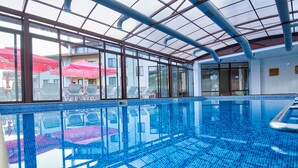 An indoor swimming pool with clear glass walls, lounge chairs, and umbrellas. - Park hotel Arbanasi (Veliko Tarnovo)