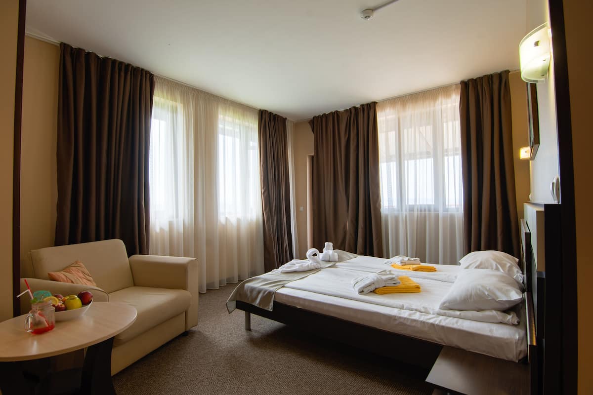 Una habitación de hotel con cama, sofá, una mesita con frutero y cortinas.