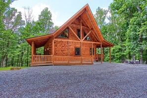 A wooden cabin with a sloped roof, a porch, and a gravel driveway.