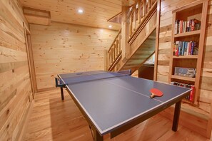 Een tafeltennistafel met een rood batje in een houten kamer met een boekenkast en een trap.