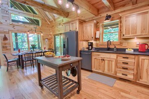 A wooden cabin interior with a dining area, kitchen, and large windows.