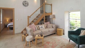 A cozy living room with a staircase, a sofa, a coffee table, and a green armchair. - Meadow Syke Barn (Penrith)