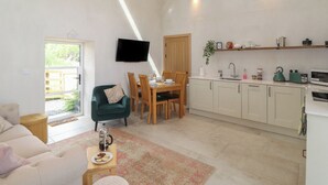 A modern kitchen with white cabinets, a dining area with wooden chairs, a green sofa, and a flat-screen TV mounted on the wall. - Meadow Syke Barn (Penrith)