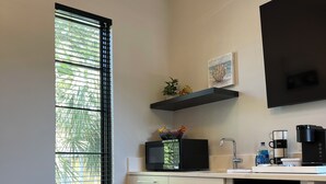 A compact kitchen with a microwave, coffee maker, and refrigerator. There is a window with blinds, a small plant on the counter, and a blue chair. - Suite A - 3 minutes walk to Center of Folly Beach, across from beach-1 Room (Folly Beach)